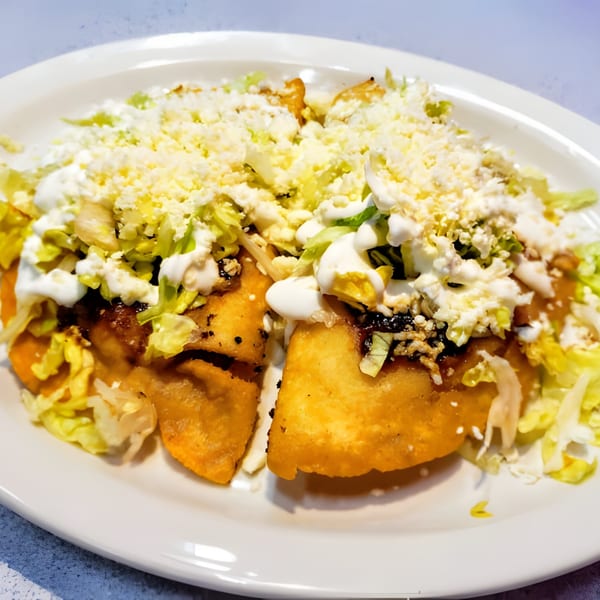 Two golden-fried Mexican sopes topped with shredded lettuce, crumbled cheese, and crema on a white plate.