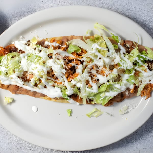 A Mexican huarache topped with refried beans, shredded meat, lettuce, sour cream, and cheese.