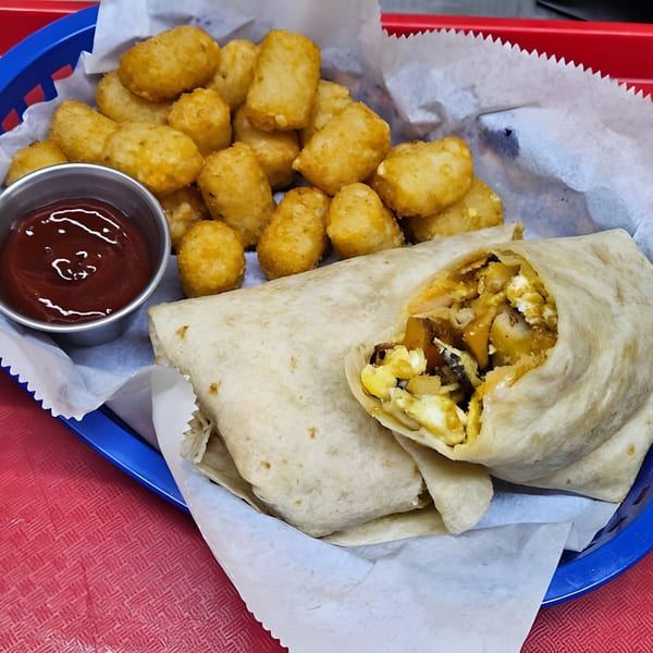A Luna's Mexican Rotisserie breakfast burrito with tater tots and ketchup in a blue basket.